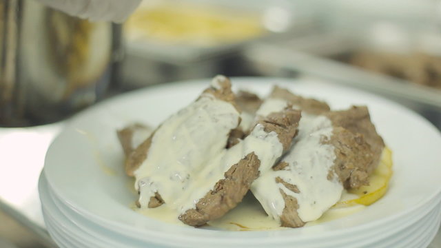 Chef puts baked apple rings and meat steak on a plate and
