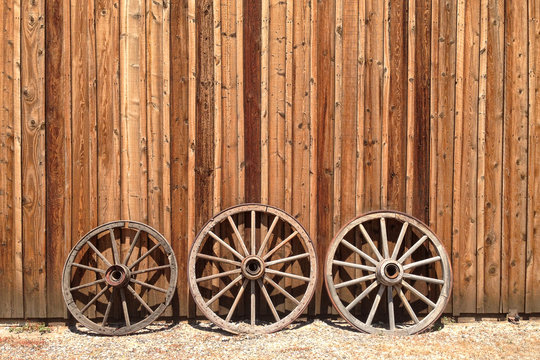 Old wagon wheels lean against a wooden barn