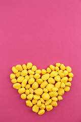 Sweet colorful candies in heart shape on pink background