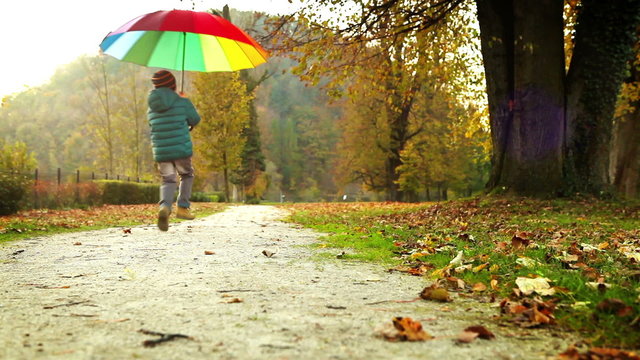 Merry little boy jumping in a park with multi-coloured umbrella