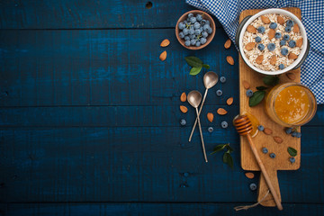 A healthy breakfast on a dark blue wooden background: Oatmeal, milk, blueberries, honey and almonds. Rustic style. - obrazy, fototapety, plakaty