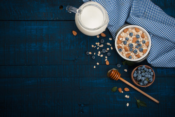 A healthy breakfast on a dark blue wooden background: Oatmeal, milk, blueberries, honey and...