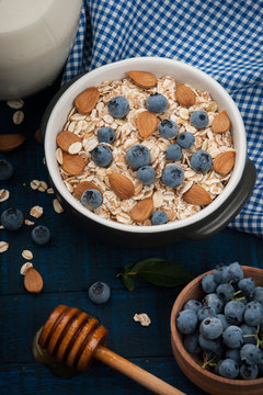 A healthy breakfast on a dark blue wooden background: Oatmeal, milk, blueberries, honey and almonds. Rustic style.