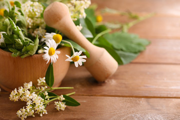 Herbs and flowers with mortar, on wooden table background