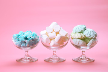 Fluffy candies in glassware on pink background