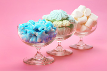 Fluffy candies in glassware on pink background