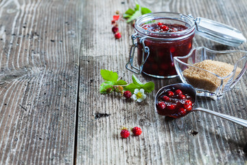 Forest strawberry jam in a jar on rustic wooden background