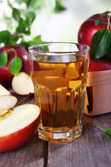 Glass of apple juice with red apples on wooden table on blurred background