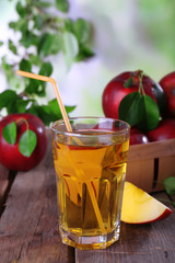 Glass of apple juice with red apples on wooden table on blurred background