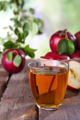 Glass of apple juice with red apples on wooden table on blurred background