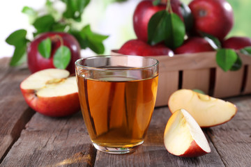 Glass of apple juice with red apples on wooden table, closeup