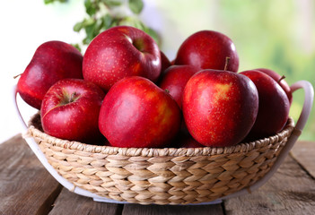 Red apple in wicker basket on wooden table on blurred background