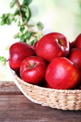 Red apple in wicker basket on wooden table on blurred background