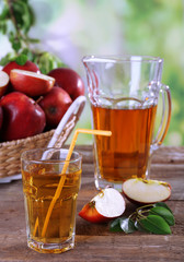Glass of apple juice with red apples on wooden table on blurred background