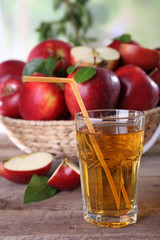 Glass of apple juice with red apples on wooden table, closeup