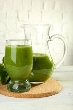 Healthy green smoothie with spinach on wooden table on white wall background