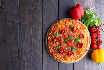 Pizza with basil and cherry tomatoes on cutting board on wooden background
