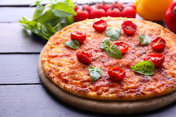 Pizza with basil and cherry tomatoes on wooden table, closeup