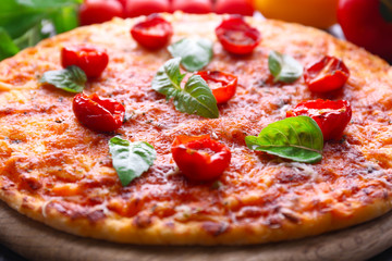 Pizza with basil and cherry tomatoes on wooden cutting board, closeup