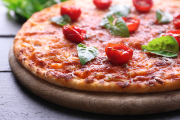 Pizza with basil and cherry tomatoes on wooden cutting board, closeup