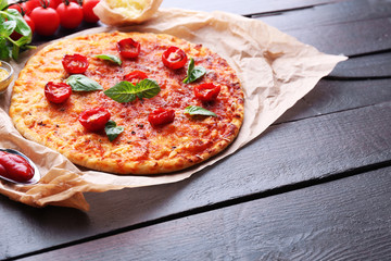 Pizza with basil and cherry tomatoes on parchment on wooden table background