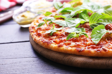 Pizza with basil on cutting board on wooden background