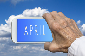 Smart phone in old hand with month of the year - April on screen