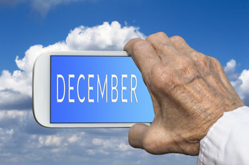 Smart phone in old hand with month of the year - December on scr