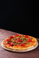 Tasty pizza with cherry tomatoes, green olives and herbs on wooden table on black background