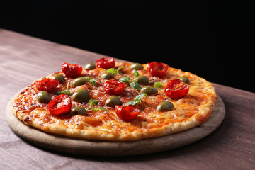 Tasty pizza with cherry tomatoes, green olives and herbs on wooden table on black background