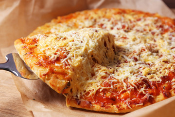 Cheese pizza on parchment with blade, closeup
