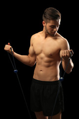 Muscle young man exercising with resistance band on dark background