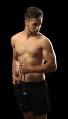 Fototapeta na wymiar Muscle young man exercising with resistance band on dark background