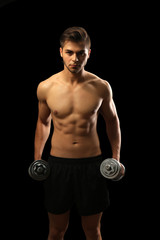 Fototapeta na wymiar Muscle young man holding dumbbells on dark background