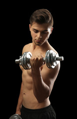 Fototapeta na wymiar Muscle young man holding dumbbell on dark background