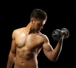 Fototapeta na wymiar Muscle young man holding dumbbell on dark background