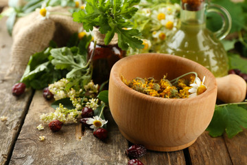 Herbs, berries and flowers with mortar, on wooden table background