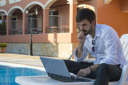 Young warried  businessman working on his laptop by the pool whi