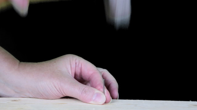 Woman's hand holding and hammering a nail on black background.