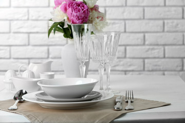 Beautiful table setting with flowers in vase on brick wall background