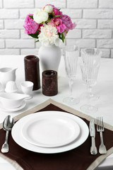 Beautiful table setting with flowers in vase on brick wall background
