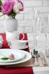 Beautiful table setting with flowers in vase on brick wall background