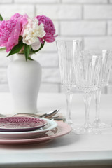 Beautiful table setting with flowers in vase on brick wall background