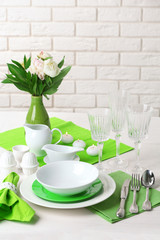 Beautiful table setting with flowers in vase on brick wall background