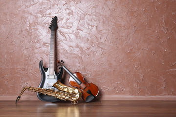 Electric guitar, saxophone and violin on brown wall background