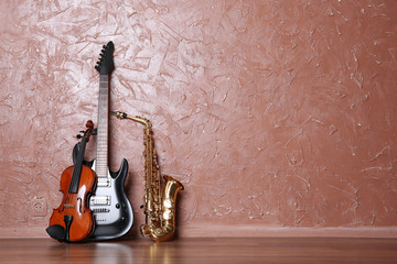 Electric guitar, saxophone and violin on brown wall background