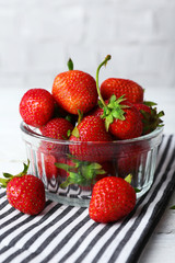 Ripe strawberries in glass saucer on napkin on wooden table, closeup