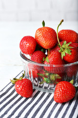 Ripe strawberries in glass saucer on napkin on wooden table, closeup