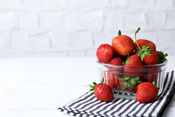 Ripe strawberries in glass saucer on napkin on wooden table on white wall background