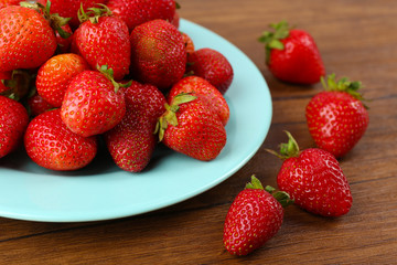 Ripe strawberries in plate on wooden table, closeup